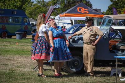 photo of a car show in the park with people standing near a car